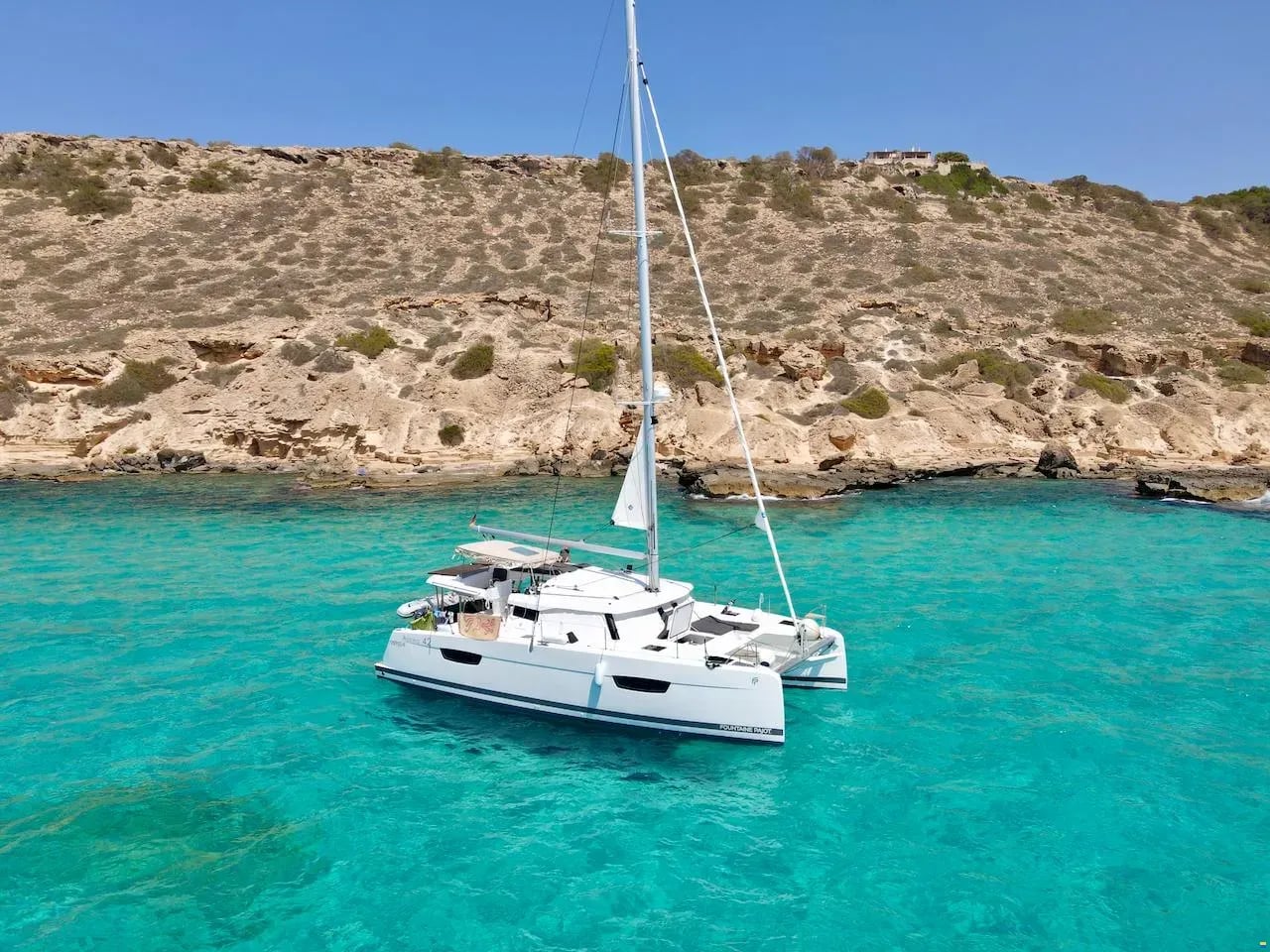 Le catamaran Astrea 42 KAHUNA au mouillage en eau turquoise au pied d'une falaise Le catamaran Astrea 42 KAHUNA au mouillage en eau turquoise au pied d'une falaise