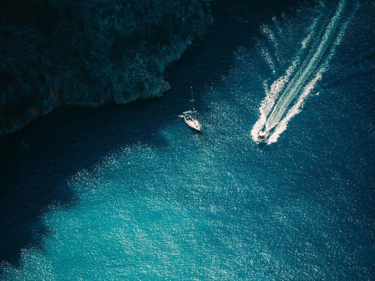 Vue aérienne d une crique méditerranéenne aux eaux turquoise, un voilier au mouillage et un bateau à moteur en navigation