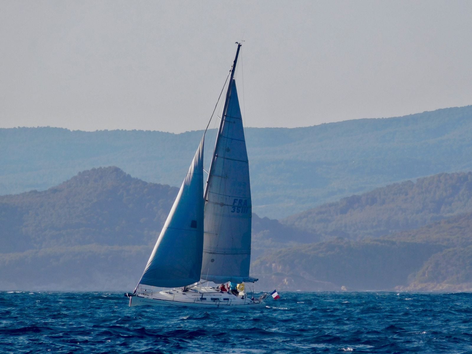 Voilier sous voiles longeant une côte de collines provençales Voilier sous voiles longeant une côte de collines provençales