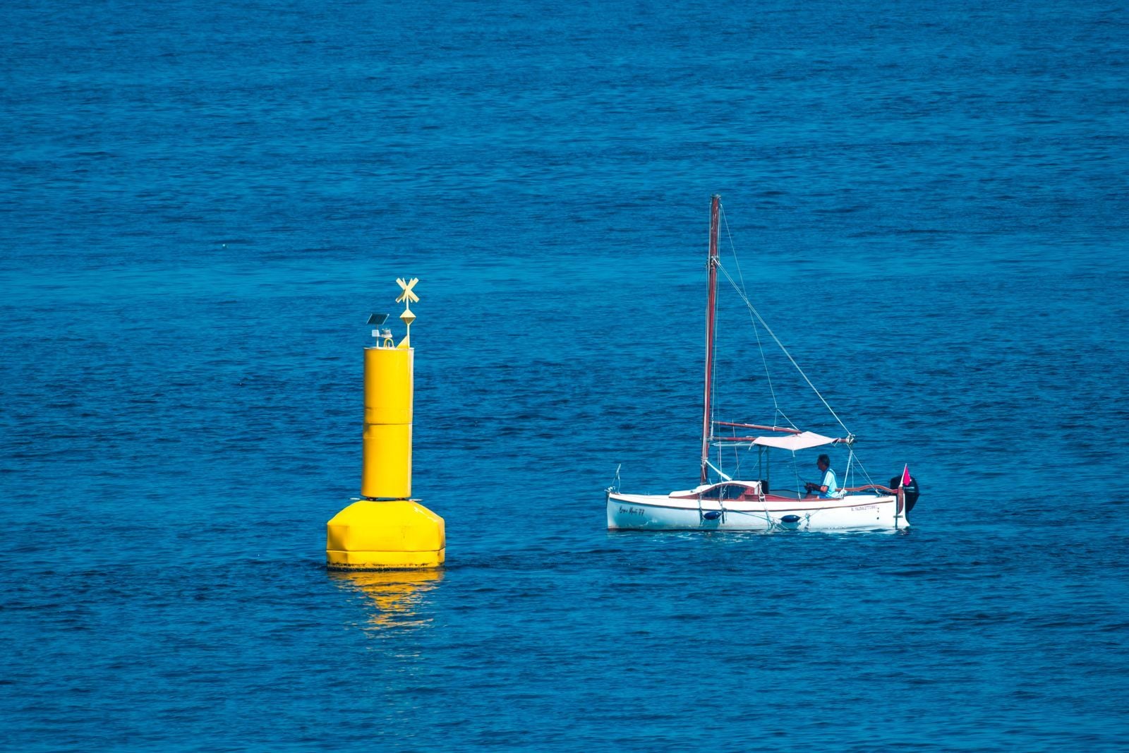 Bouée jaune de balisage en mer, un petit voilier passe à côté Bouée jaune de balisage en mer, un petit voilier passe à côté